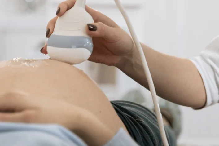 Een echoscopist houdt de echokop op de buik van een zwangere vrouw die ontspannen op de behandelbank ligt
