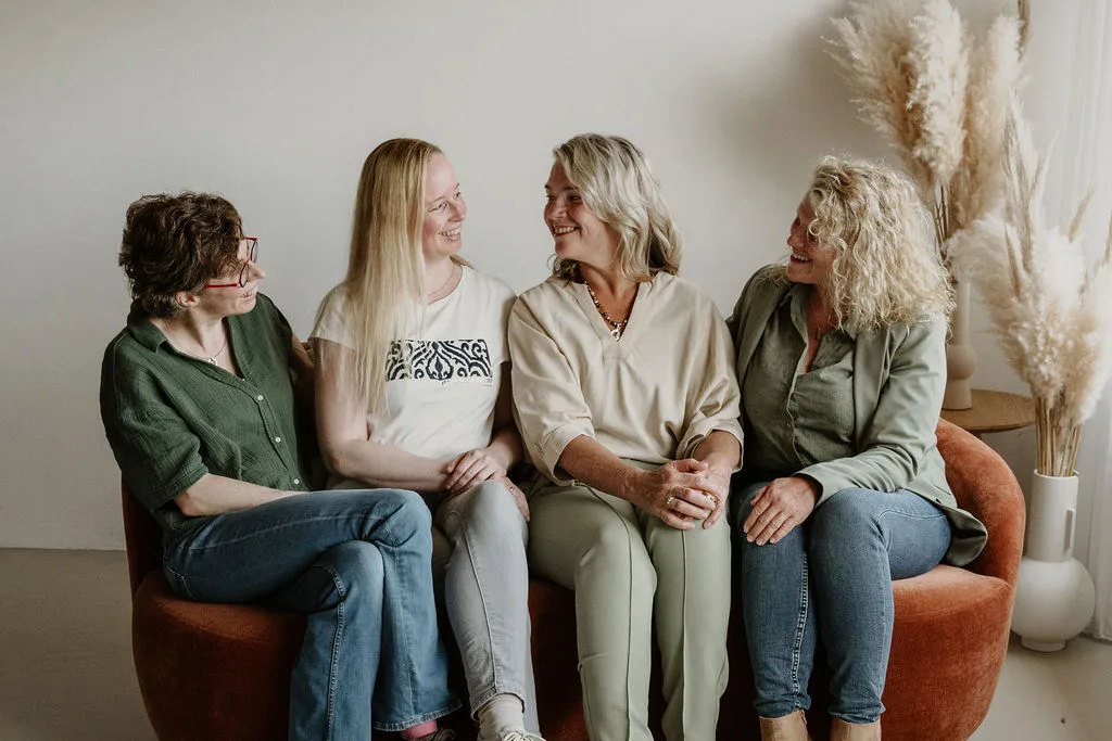 De echoscopisten Deborah, Joan en Evelien en assistente Ineke zitten op een bank en kijken elkaar lachend aan