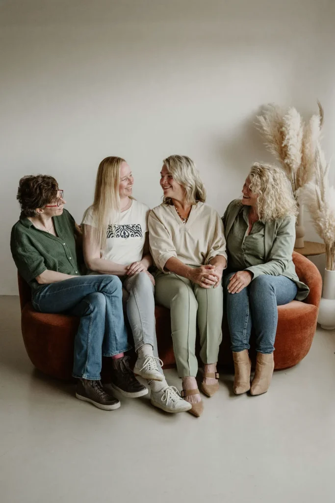 De echoscopisten Deborah, Joan en Evelien en assistente Ineke zitten lachend naast elkaar op een roestbruine bank